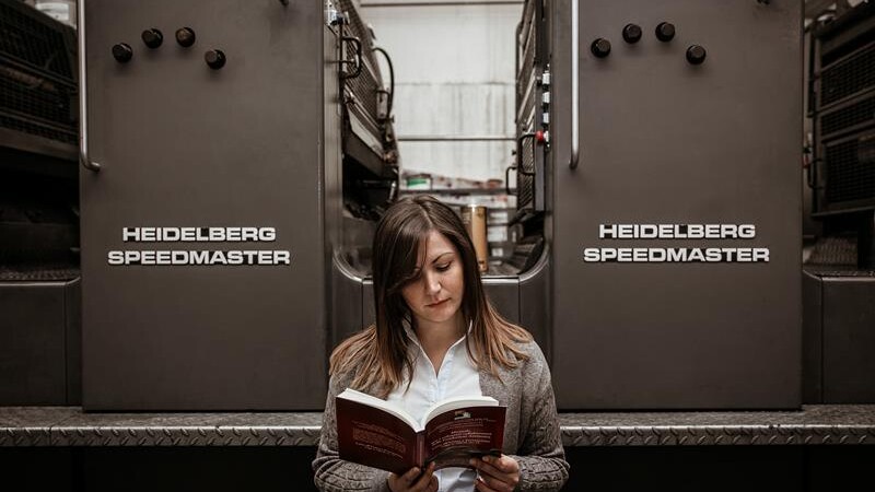 donna che legge un libro con heidelberg speedmaster alle sue spalle