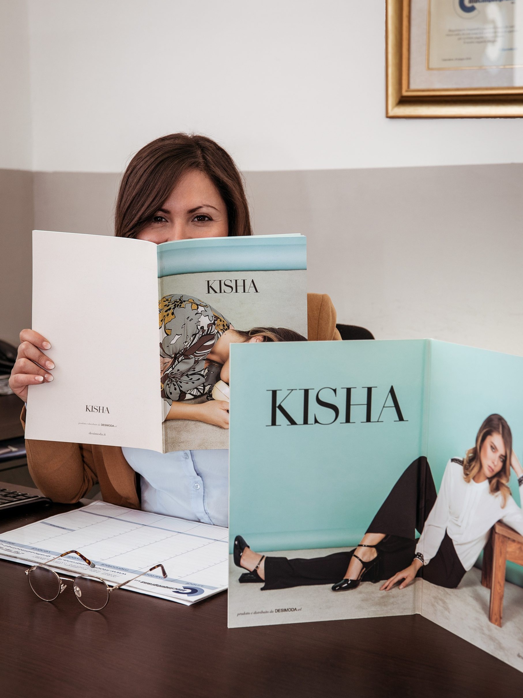 woman sitting in her office hiding her face with a fashion catalogue
