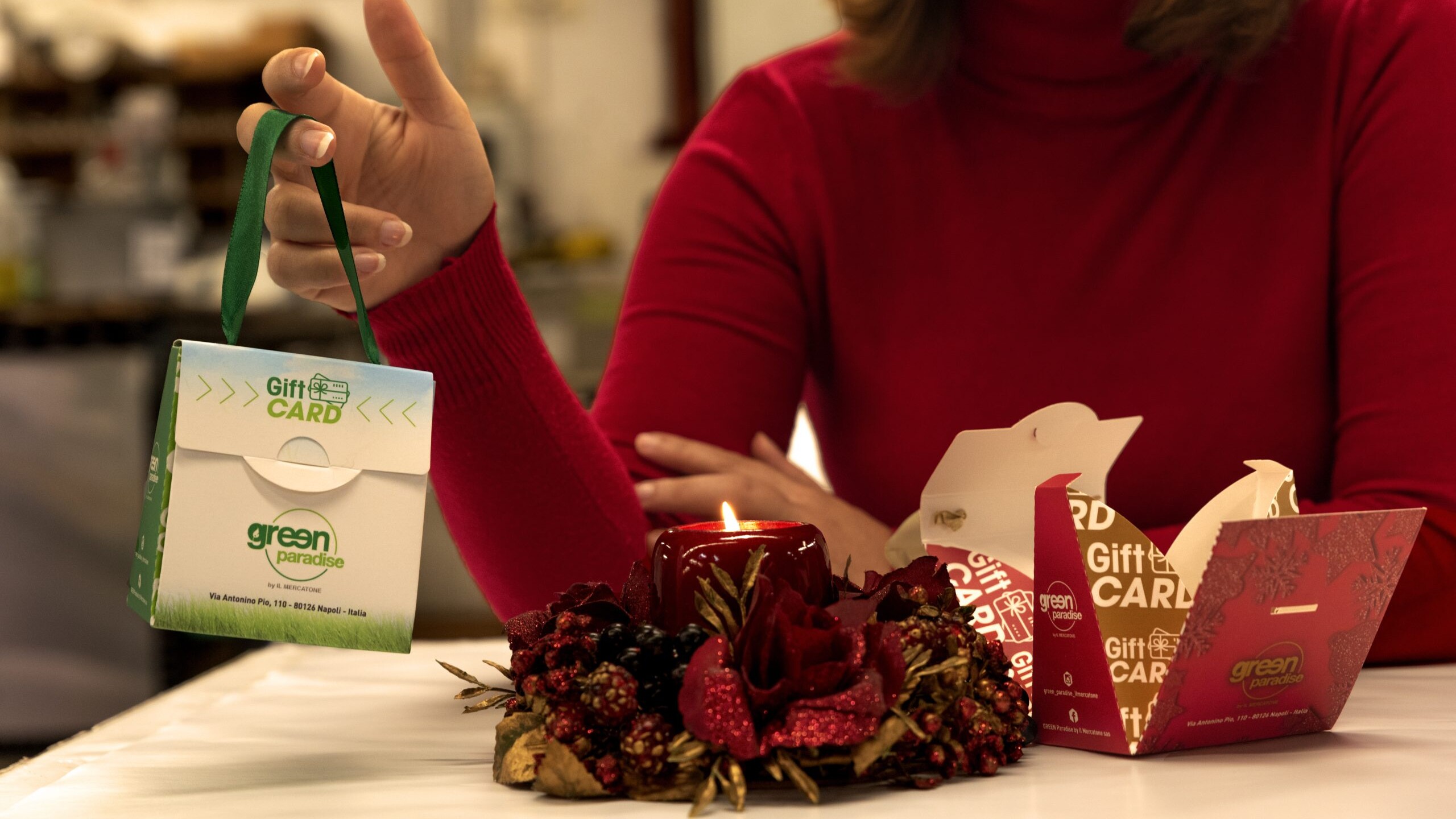 packaging verde vicino a candela rossa natalizia tenuto tra le mani di una donna