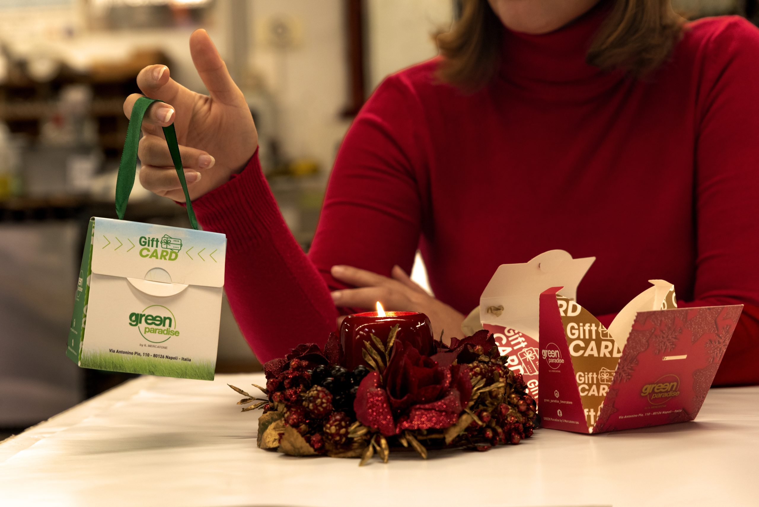 packaging verde vicino a candela rossa natalizia tenuto tra le mani di una donna